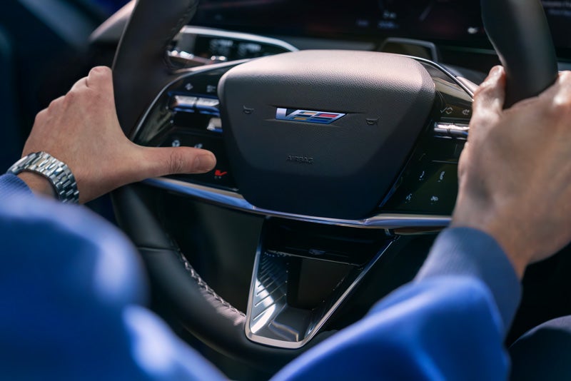 Close-up of a Man About to Press the V-Button on the 2026 OPTIQ-V Steering Wheel | McLaughlin Cadillac in Moline IL